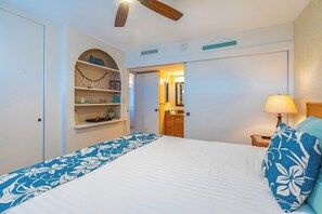 A bedroom with a bed, a nightstand, a lamp, a ceiling fan, and a door leading to a bathroom.