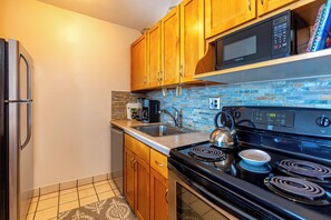 A kitchen with wooden cabinets, a stainless steel refrigerator, a microwave, a stove, and a brick backsplash.