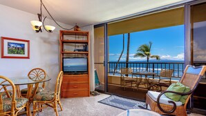 A balcony with a view of the ocean, wicker furniture, a glass table, and a bookshelf. - Beachfront Paradise with A/C - Sugar Beach Resort #227 - Stunning Ocean Views! (Kihei, Maui)