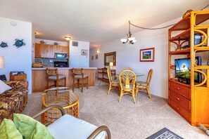 A compact living space with a kitchenette, dining area, and a cozy seating area with wicker furniture. - Beachfront Paradise with A/C - Sugar Beach Resort #227 - Stunning Ocean Views! (Kihei, Maui)