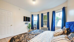 Een slaapkamer met een bed, een televisie, een raam met gordijnen en een radiator.