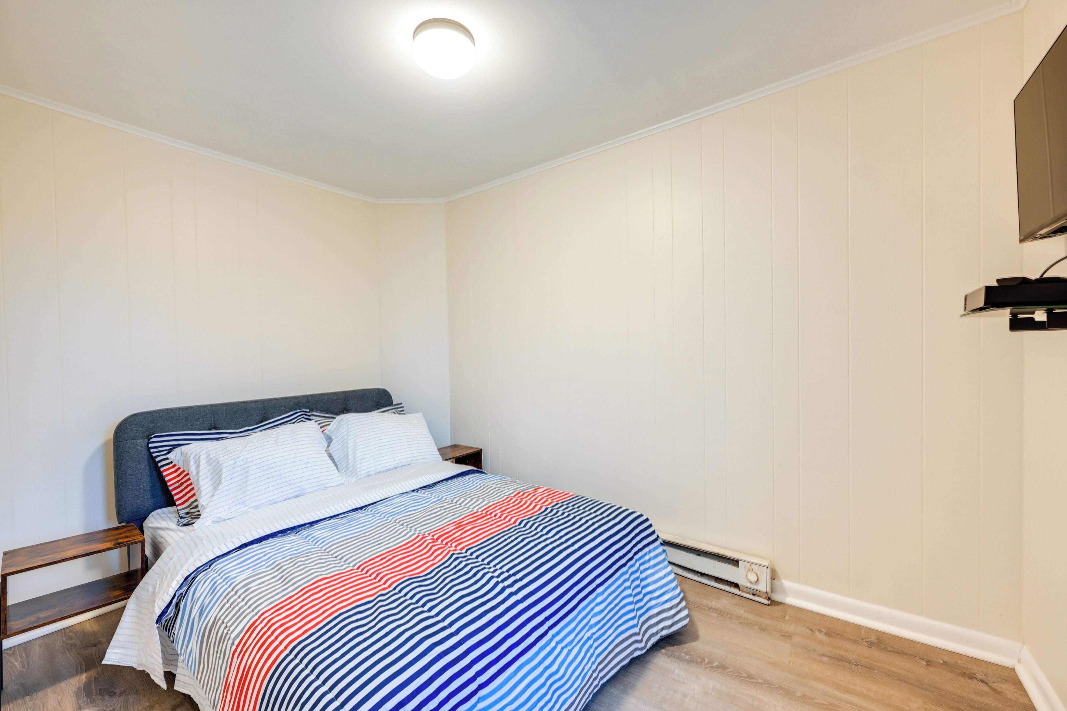 Une chambre à coucher comprenant un lit, une table de chevet, un téléviseur fixé au mur et un luminaire au plafond.
