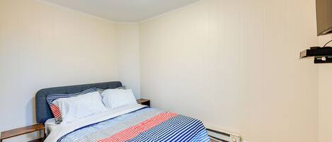 A bedroom with a bed, a nightstand, a wall-mounted TV, and a ceiling light.