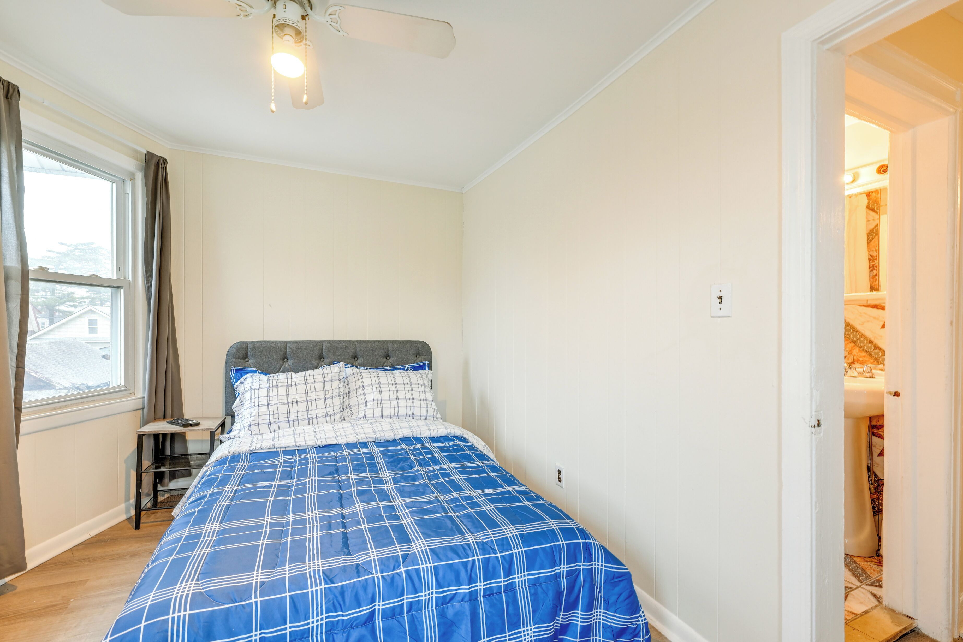 A bedroom with a bed, a window, a ceiling fan, and a door leading to a bathroom.