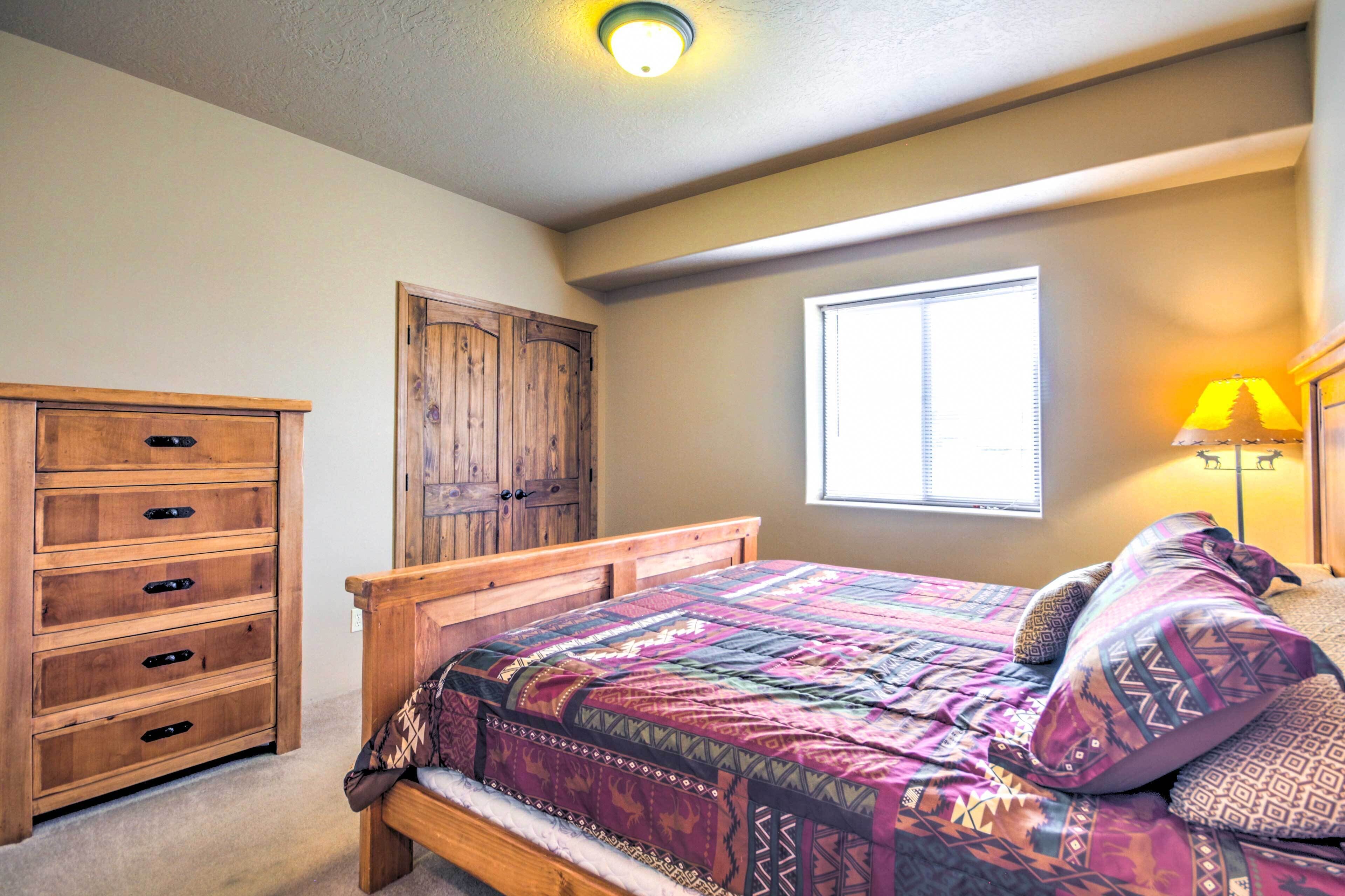 A bedroom with a wooden bed, a dresser, a window with blinds, and a lamp.