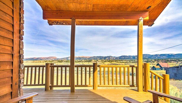 Una terraza de madera con bancos, con vistas a un paisaje rural con montañas y casas.