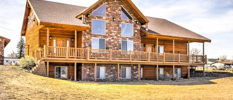 A two-story log cabin with a balcony, large windows, and a chimney.