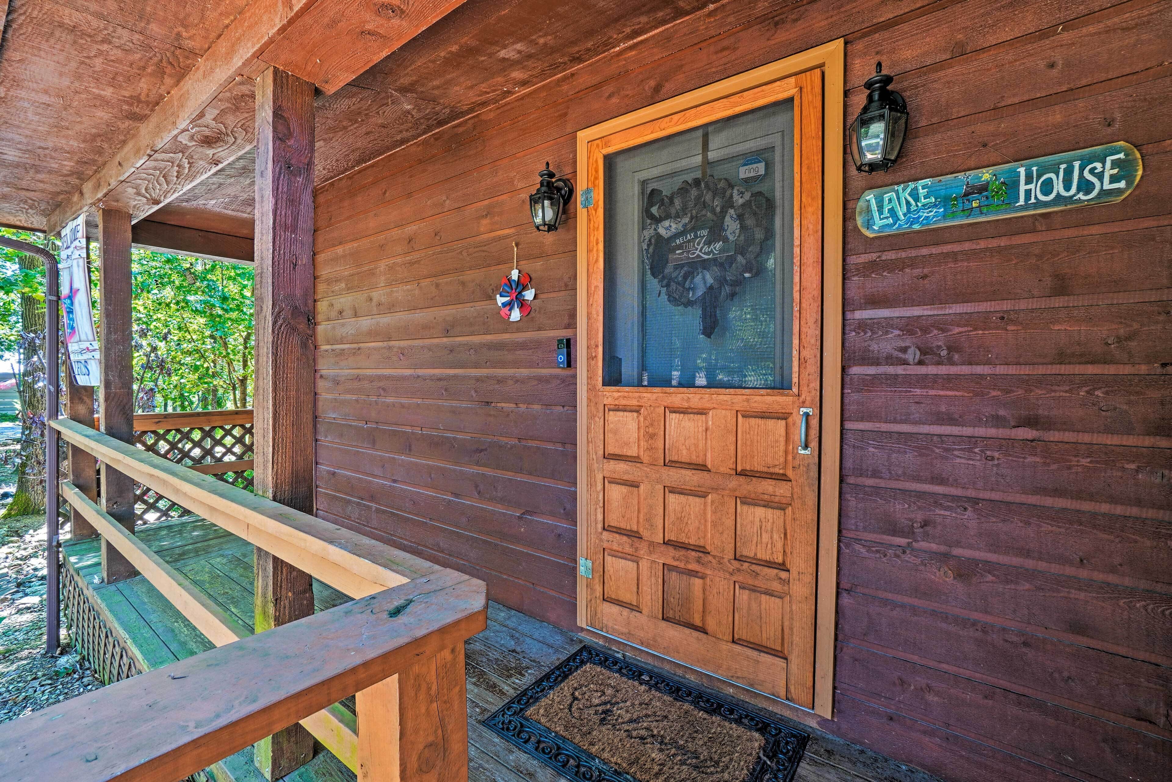 Eine Holzhütte mit Holztür, einer Bank, einer Fußmatte und einem Schild mit der Aufschrift 'Lake House'.