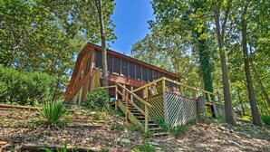 A rustic cabin with a wooden staircase leading up to a deck, surrounded by dense forest. - Home w/ Large Deck on Table Rock Lake! (Golden)