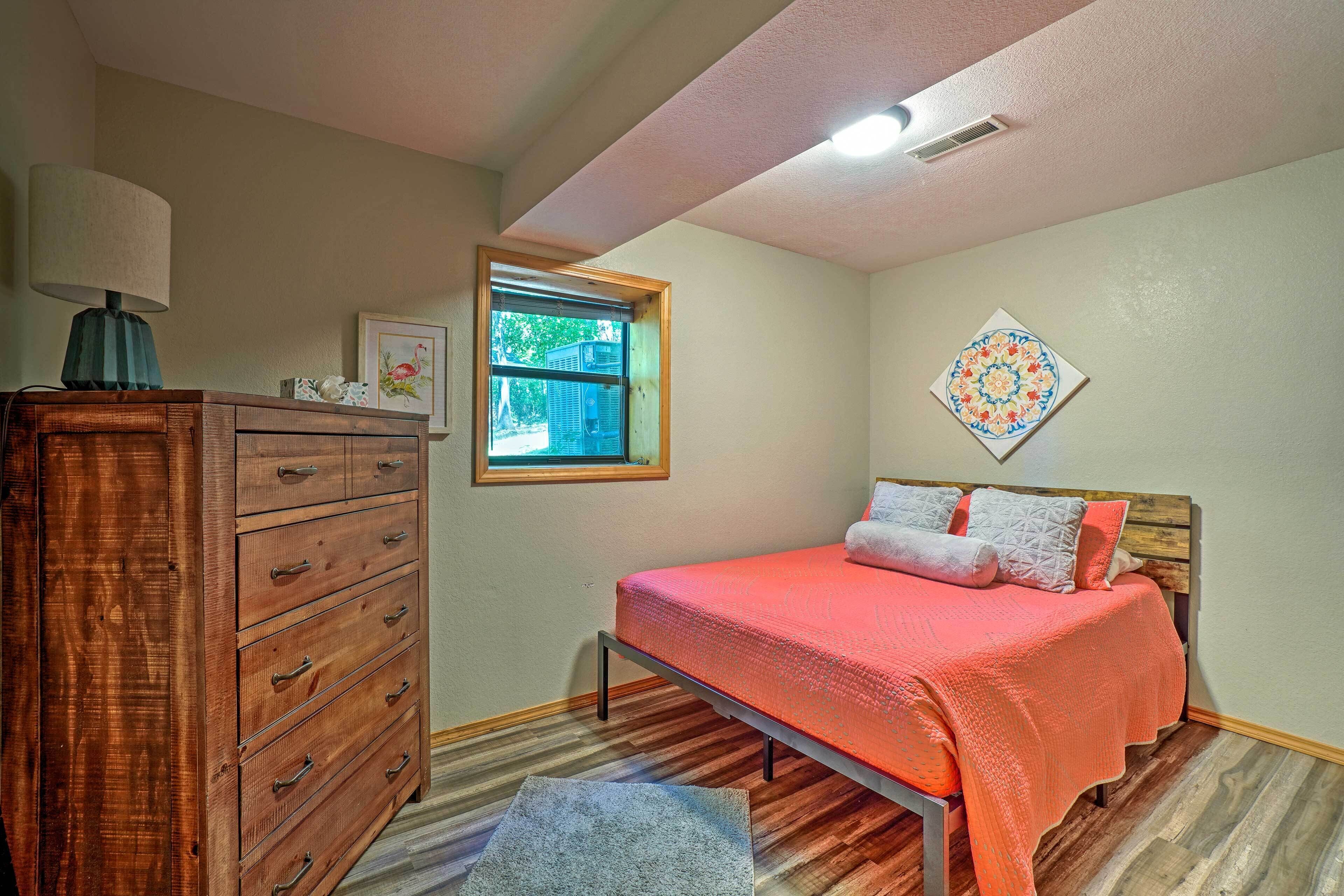 A bedroom with a wooden dresser, a bed with an orange bedspread, a window, and a wall-mounted decorative plate.
