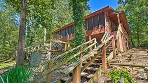 A wooden cabin with a staircase leading to a deck, surrounded by trees and greenery. - Home w/ Large Deck on Table Rock Lake! (Golden)