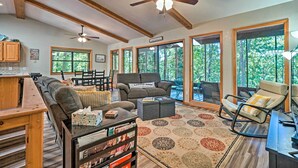 A spacious living room with a large sofa, a coffee table, and a fireplace. There are multiple windows providing natural light and views of the outdoors. - Home w/ Large Deck on Table Rock Lake! (Golden)