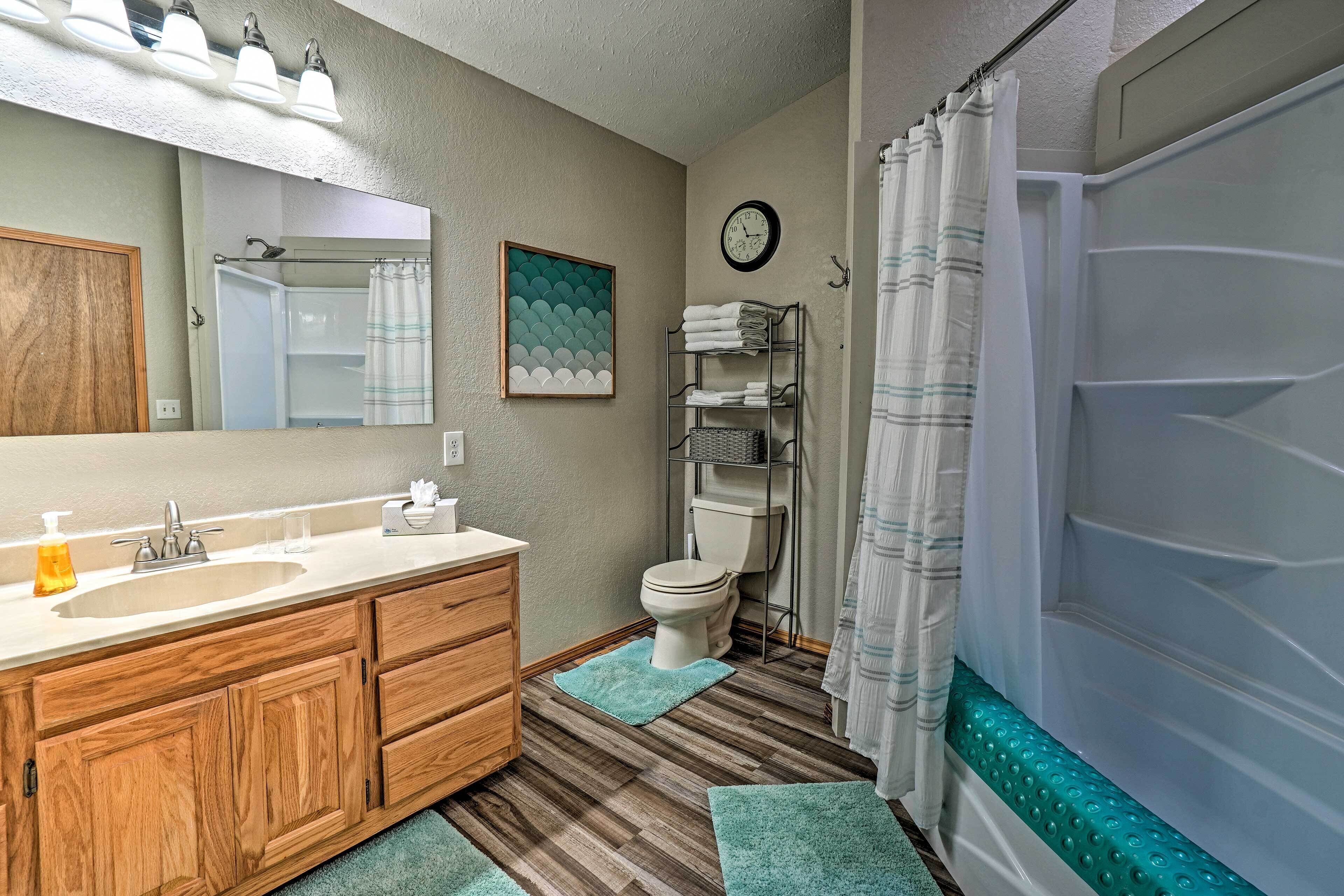 Un baño con tocador de madera, lavamanos, espejo, inodoro y ducha con cortina.