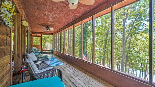 A covered porch with wicker furniture, a ceiling fan, and large windows overlooking a forest. - Home w/ Large Deck on Table Rock Lake! (Golden)