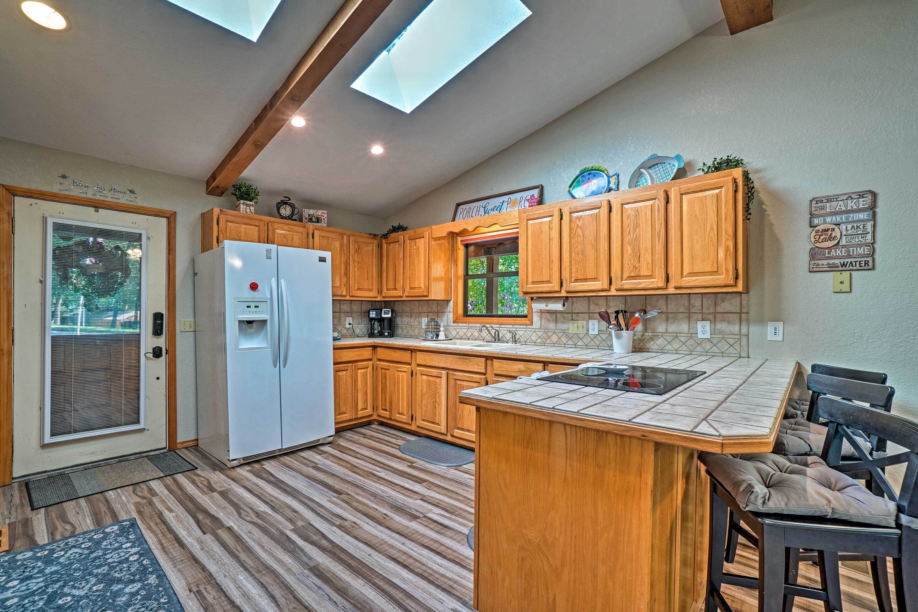 Una cocina con armarios de madera, un refrigerador blanco, una isla integrada con un fregadero y una ventana con vistas a la vegetación.