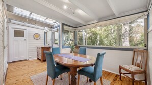 Un coin repas avec une table en bois, quatre chaises et une vue sur les arbres à travers de grandes fenêtres.