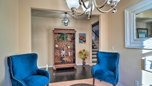 A living room with two blue velvet armchairs, a dark wooden coffee table, a decorative metal cabinet, and a chandelier. - Pet-friendly Parker House Rental w/ Home Gym! (Parker)