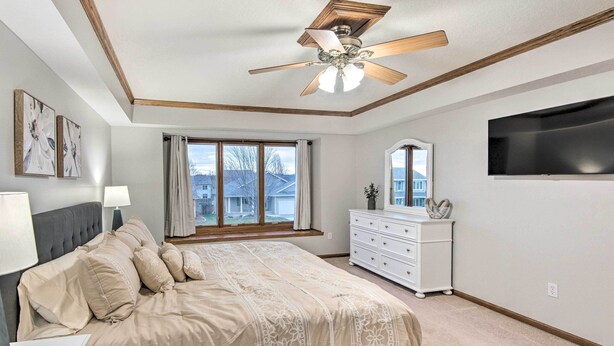 Une chambre à coucher comprenant un lit, une commode, un ventilateur de plafond, un téléviseur et une fenêtre avec des rideaux.