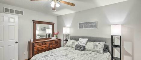 A bedroom with a bed, dresser, mirror, ceiling fan, bedside lamps, and a wall sign.