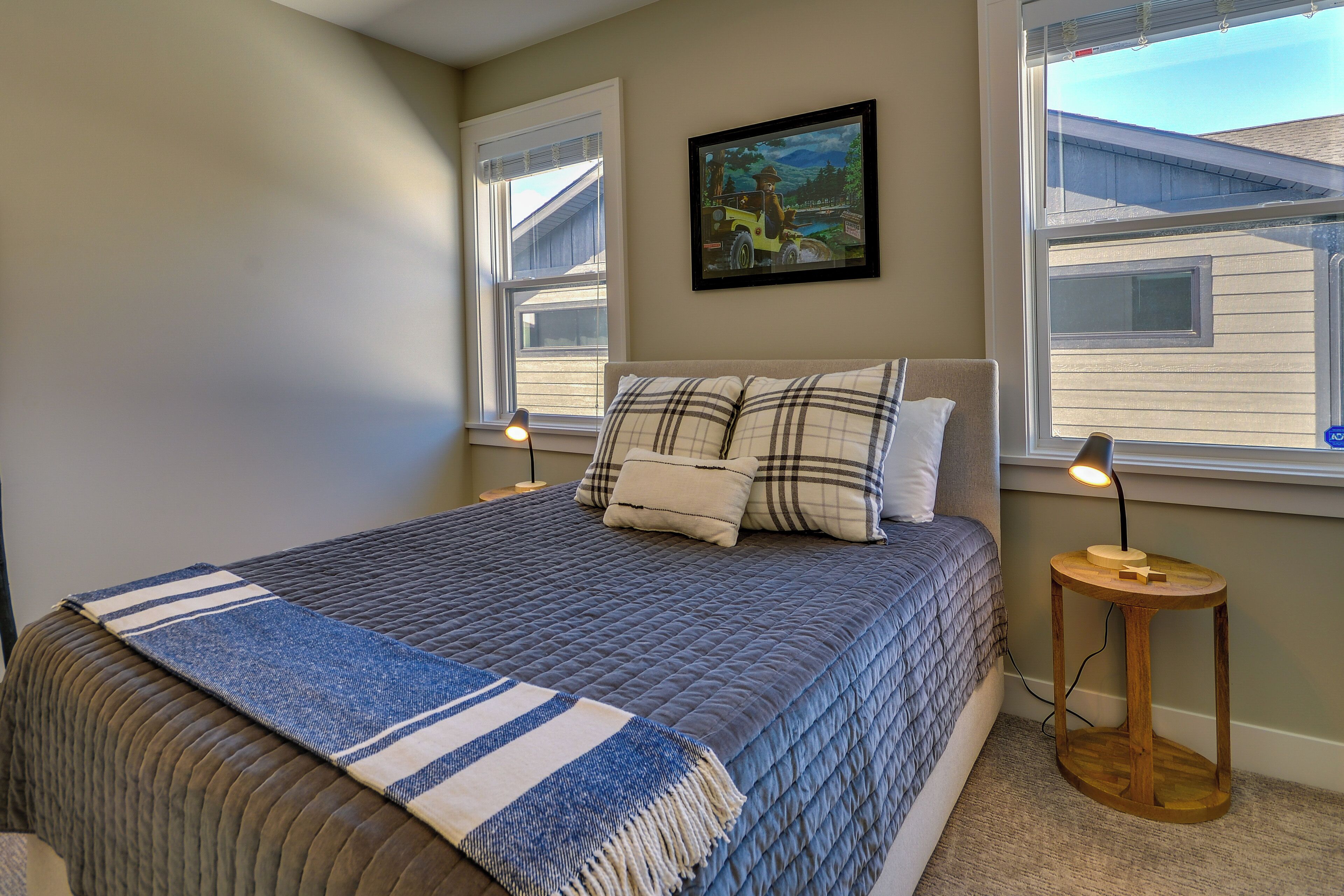 A bedroom with a large bed, two bedside lamps, a painting on the wall, and a window with blinds.