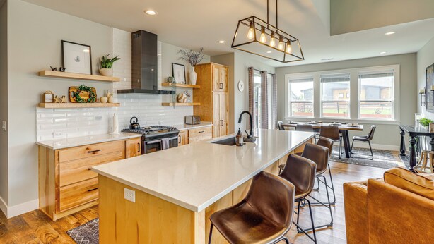 A modern kitchen with a large island, wooden cabinets, and a dining area with bar stools. - Stylish Montana Vacation Rental w/ Private Hot Tub (Red Lodge)