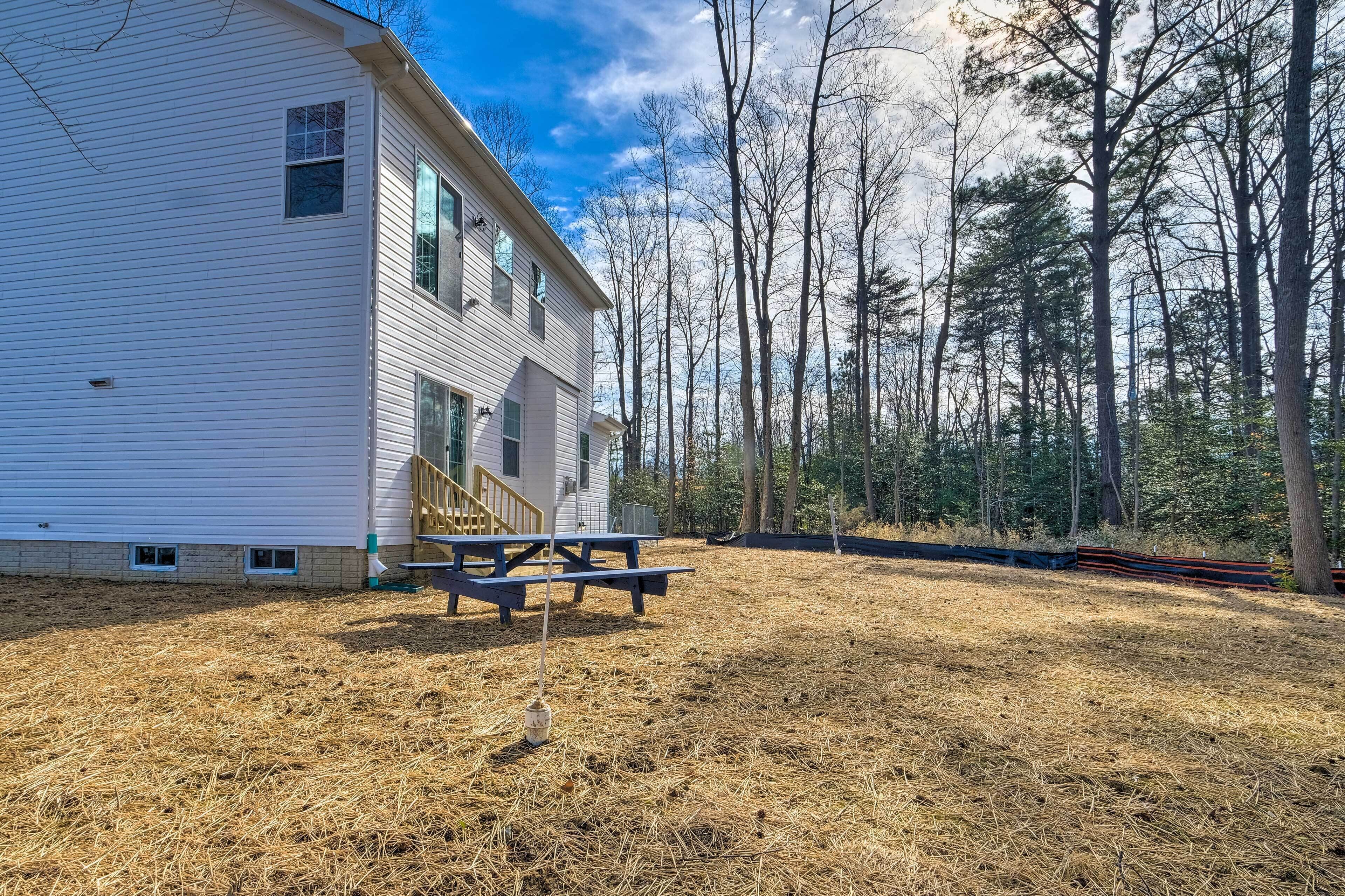 A white house with a wooden deck and picnic table, surrounded by a forested area.