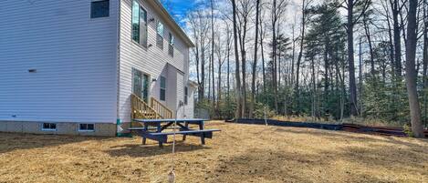 A white house with a wooden deck and picnic table, surrounded by a forested area.