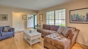 A living room with a brown sectional sofa, a blue sofa, and a white coffee table. There are framed pictures on the walls and a window with blinds. - 8 Mi to Lake Ray Hubbard: Creekside Garland Home (Garland)