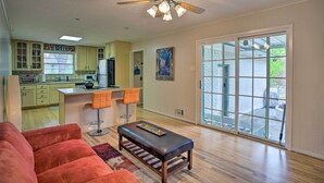 A spacious living area with a red sofa, a wooden bench, and a ceiling fan. - 8 Mi to Lake Ray Hubbard: Creekside Garland Home (Garland)