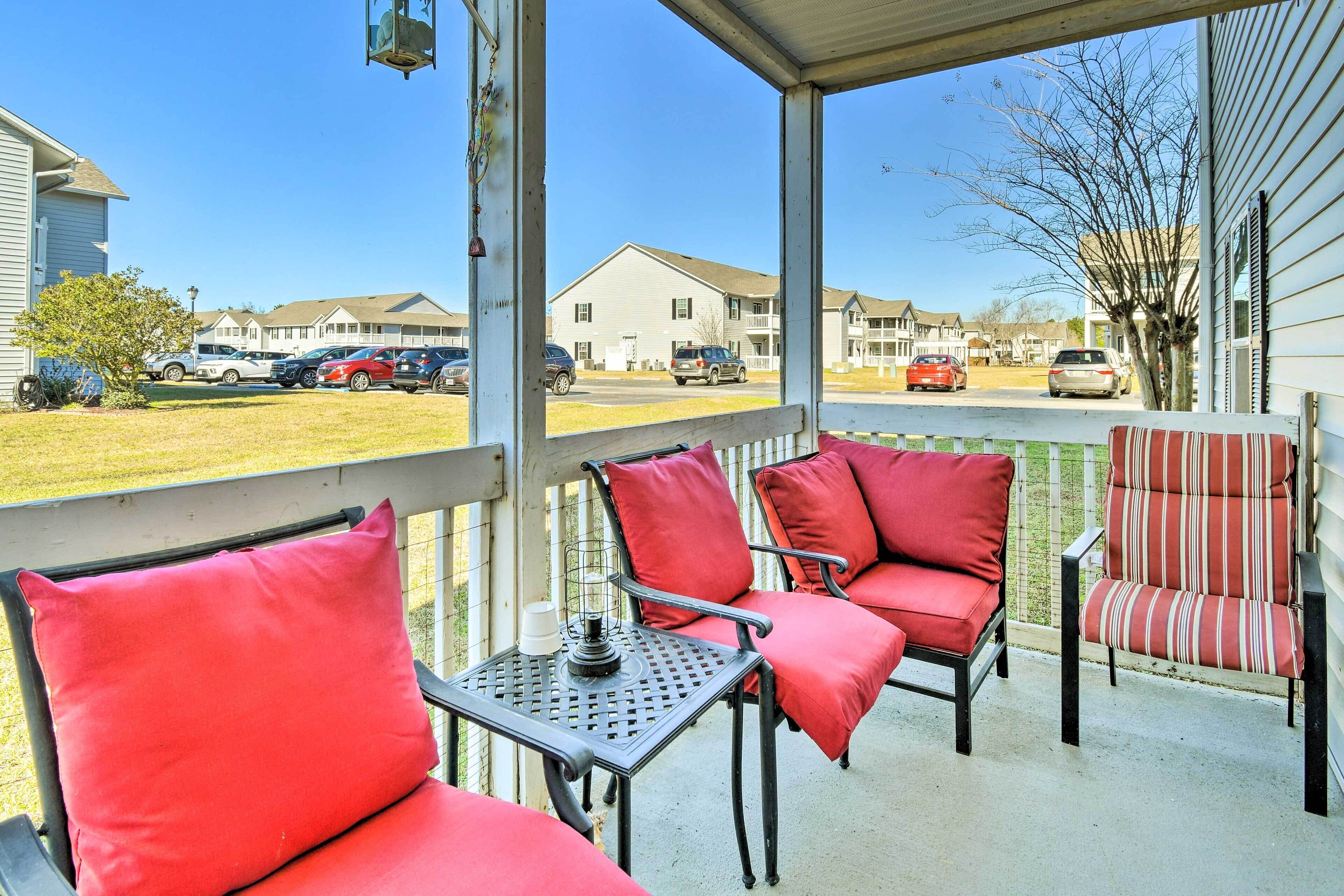 A covered porch with red cushioned chairs and a table, overlooking a residential street.