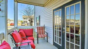 A covered porch with a seating area, a table with a drink, and a door leading to a garage.