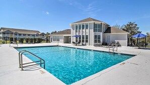A swimming pool with a metal ladder, lounge chairs, and umbrellas.