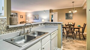 A kitchen with two sinks, a dining area with a wooden table and chairs, and a hallway with a door.