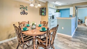 A dining area with a wooden table and chairs, a chandelier, and a kitchen in the background.