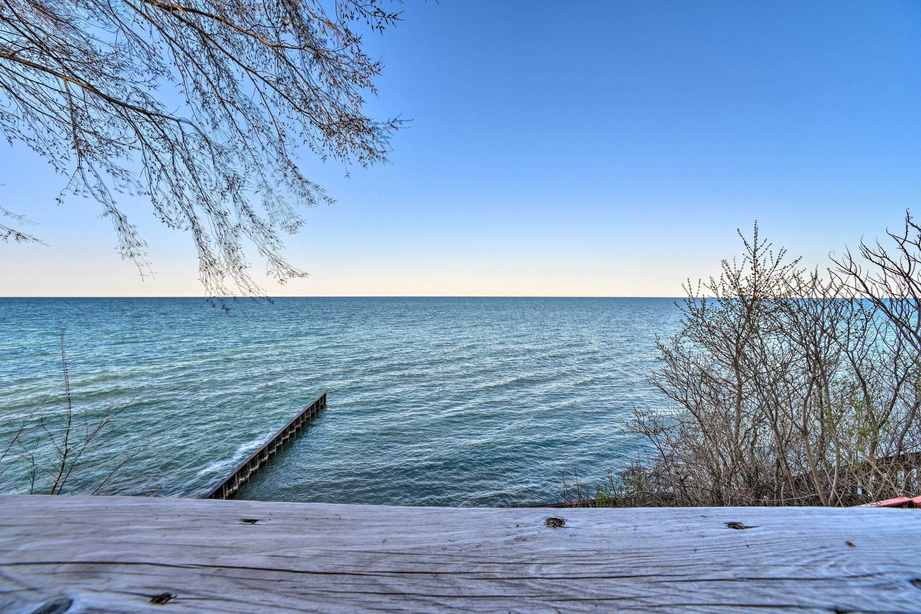 Eine Holzstele ragt in ruhiges Wasser unter einem wolkenlosen Himmel.