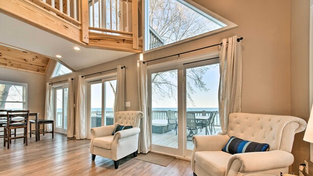 Un salon spacieux avec un haut plafond, des poutres en bois, de grandes fenêtres et une vue sur la mer.