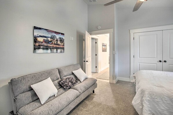 Een slaapkamer met een grijze bank, een wit bed en een schilderij van een landschap aan de muur.
