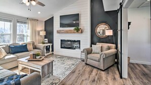 A modern living room with a fireplace, a mounted TV, and a ceiling fan. - 'the Retreat on Reno' Home w/ Hot Tub + Deck! (Reeds Spring)