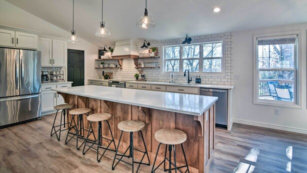 A modern kitchen with a large island, bar stools, stainless steel appliances, and pendant lighting. - 'the Retreat on Reno' Home w/ Hot Tub + Deck! (Reeds Spring)