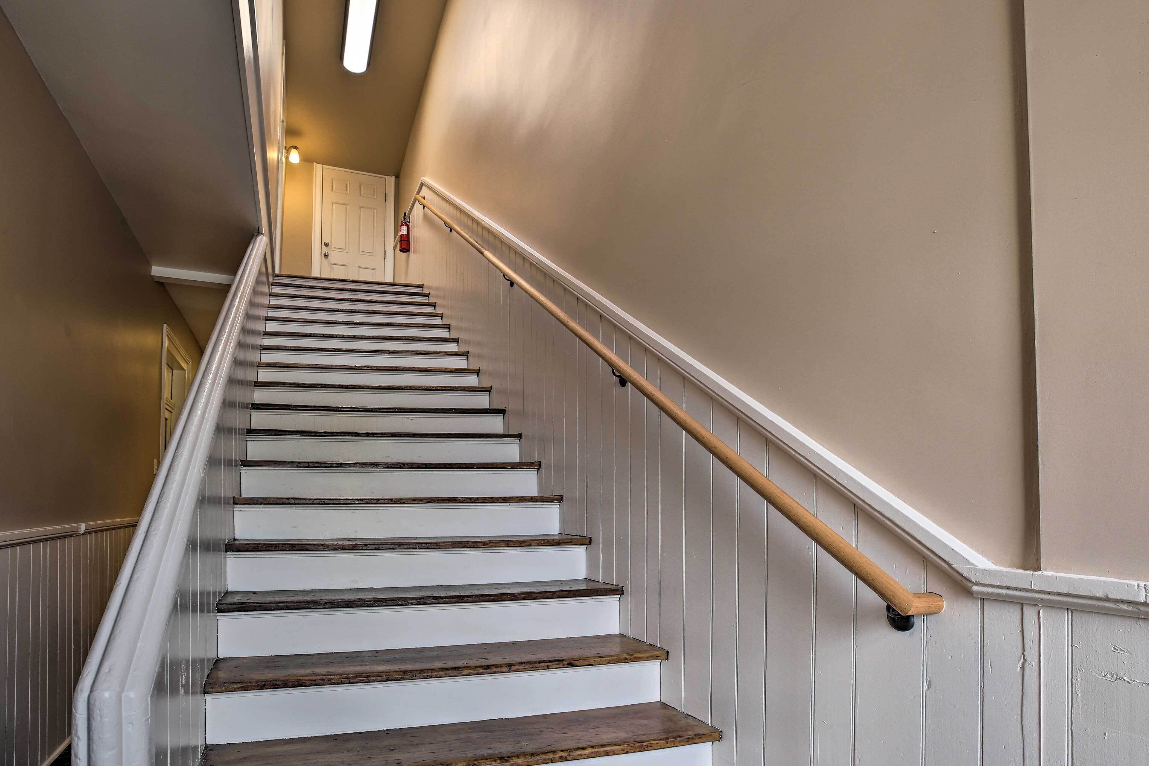 Un escalier avec des marches peintes en blanc et une rampe en bois, menant à une porte située en haut.