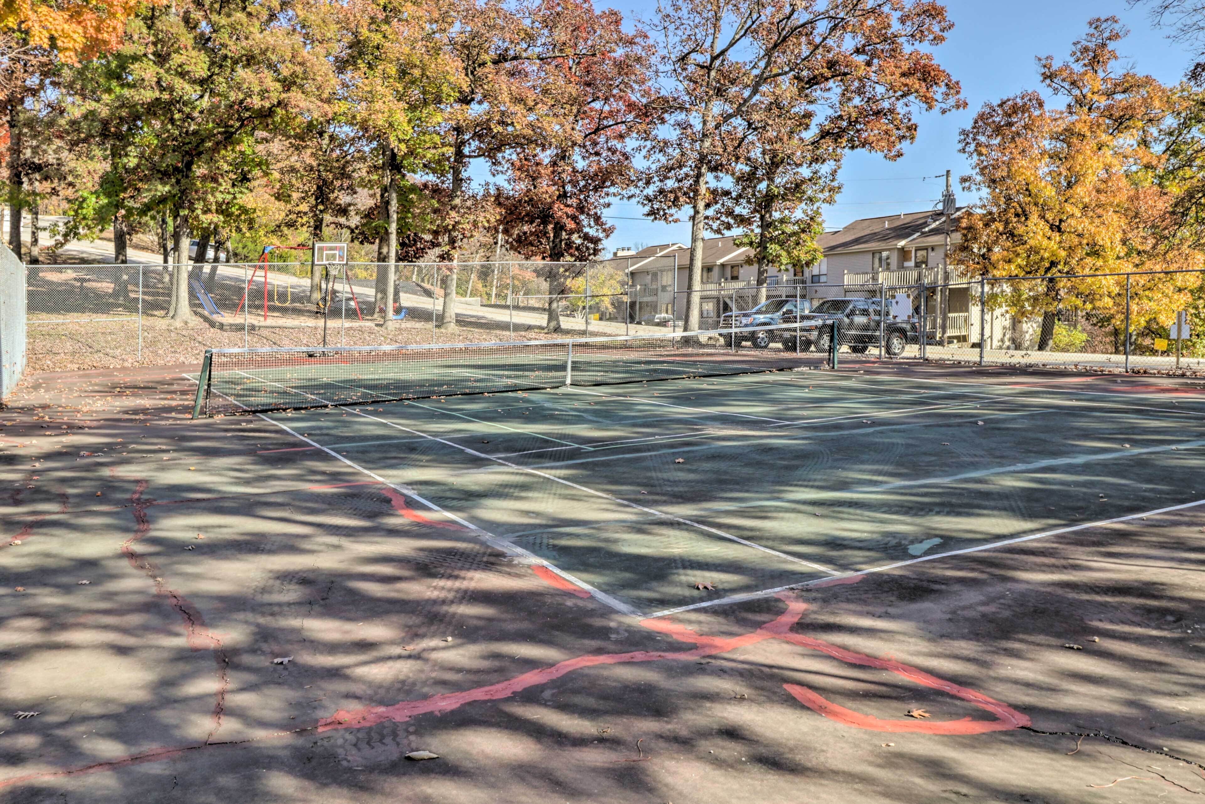 Cancha de tenis exterior con red, rodeada de árboles con follaje otoñal.