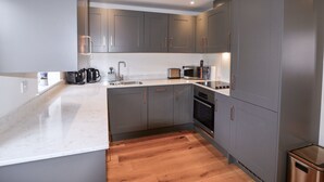 Uma cozinha moderna com armários cinza, bancada branca e piso de madeira.