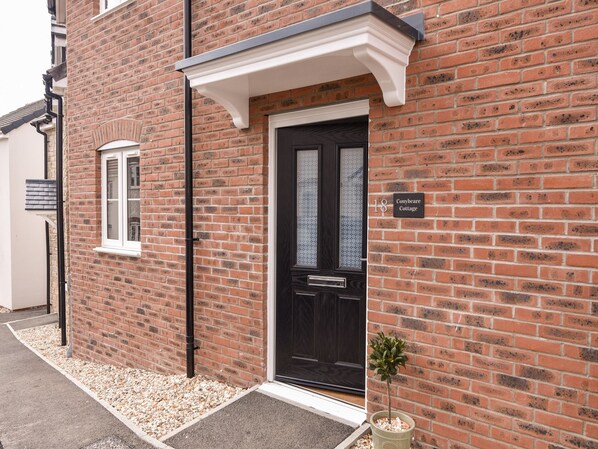A brick building with a black door, a small window, and a sign indicating '18 Conybeare Cottage'. - Conybeare Cottage (Lyme Regis)