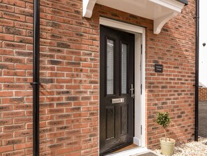 A brick building with a dark door, a small potted plant, and a sign indicating the address. - Conybeare Cottage (Lyme Regis)