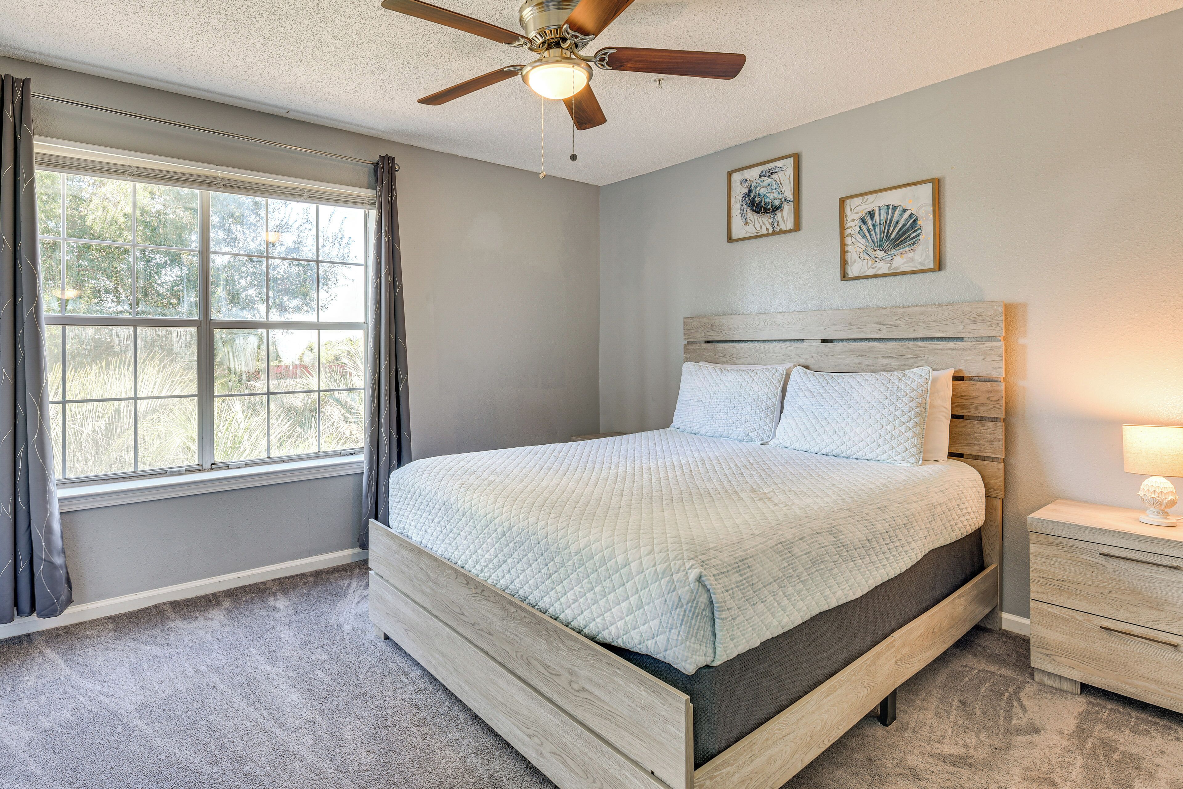 A bedroom with a bed, a nightstand, a ceiling fan, and a window with curtains.