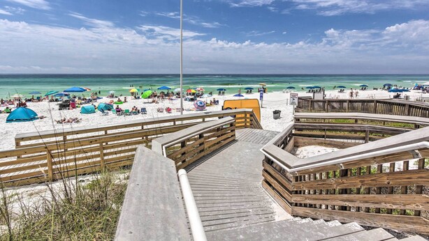 A beach with wooden walkways, tents, and umbrellas. - Explore Boardwalk Thrills! Central Destin Condo (Destin)