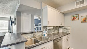 A modern kitchen with white cabinets, a granite countertop, stainless steel sink, and a dishwasher. - Explore Boardwalk Thrills! Central Destin Condo (Destin)
