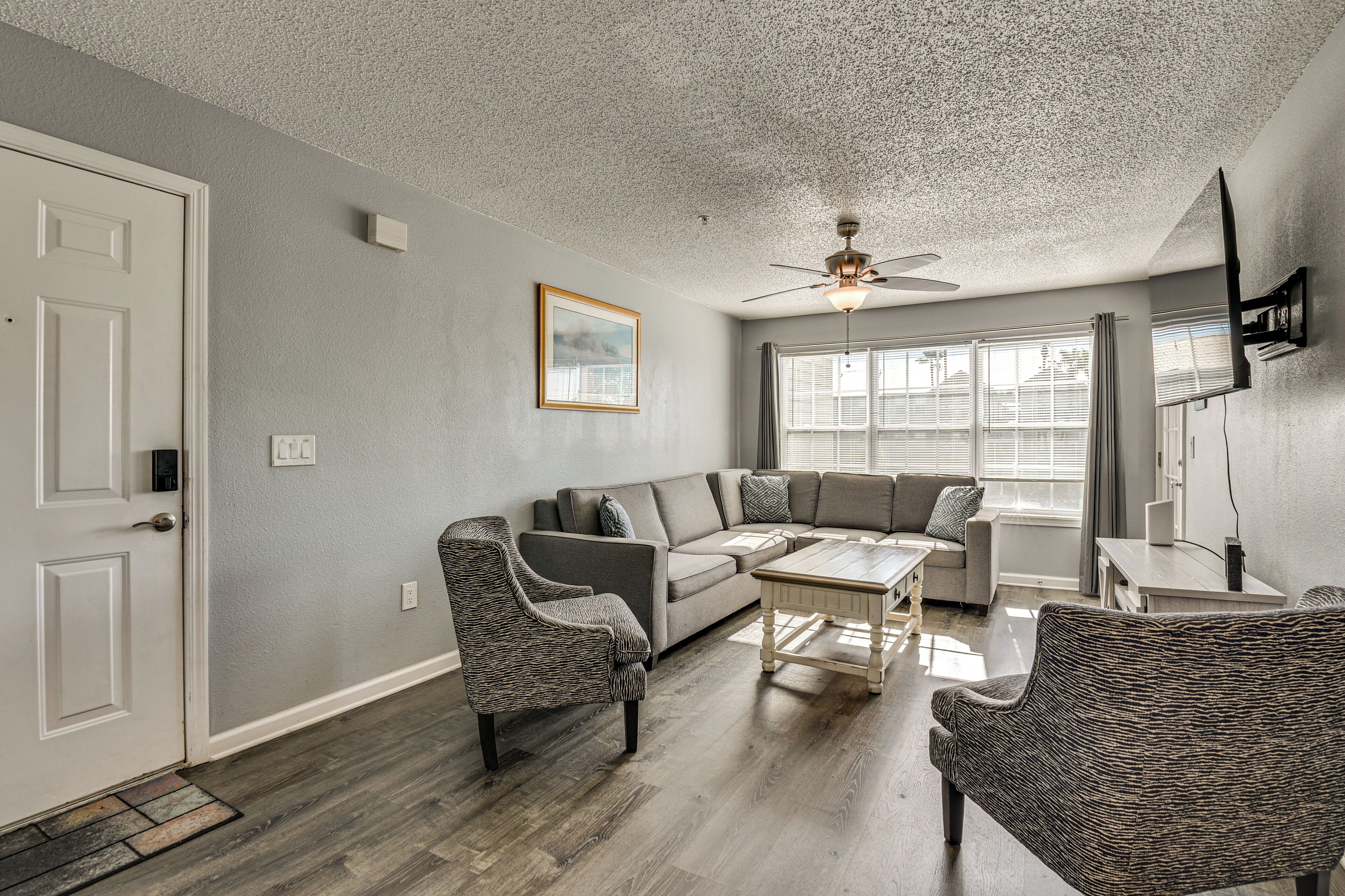 A living room with a gray sofa, two wicker chairs, a coffee table, and a ceiling fan.