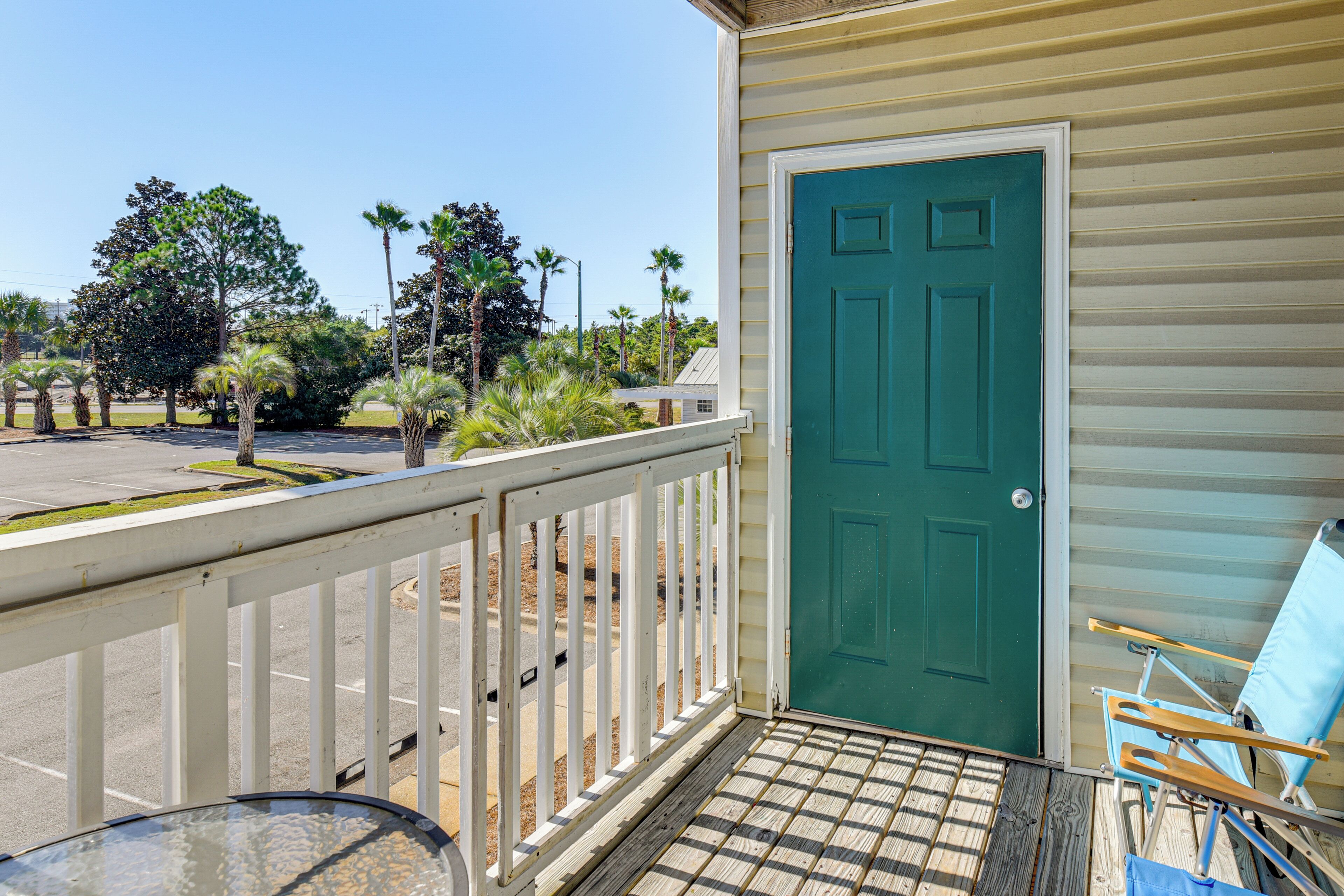 A porch with a green door, a white railing, and a blue chair.
