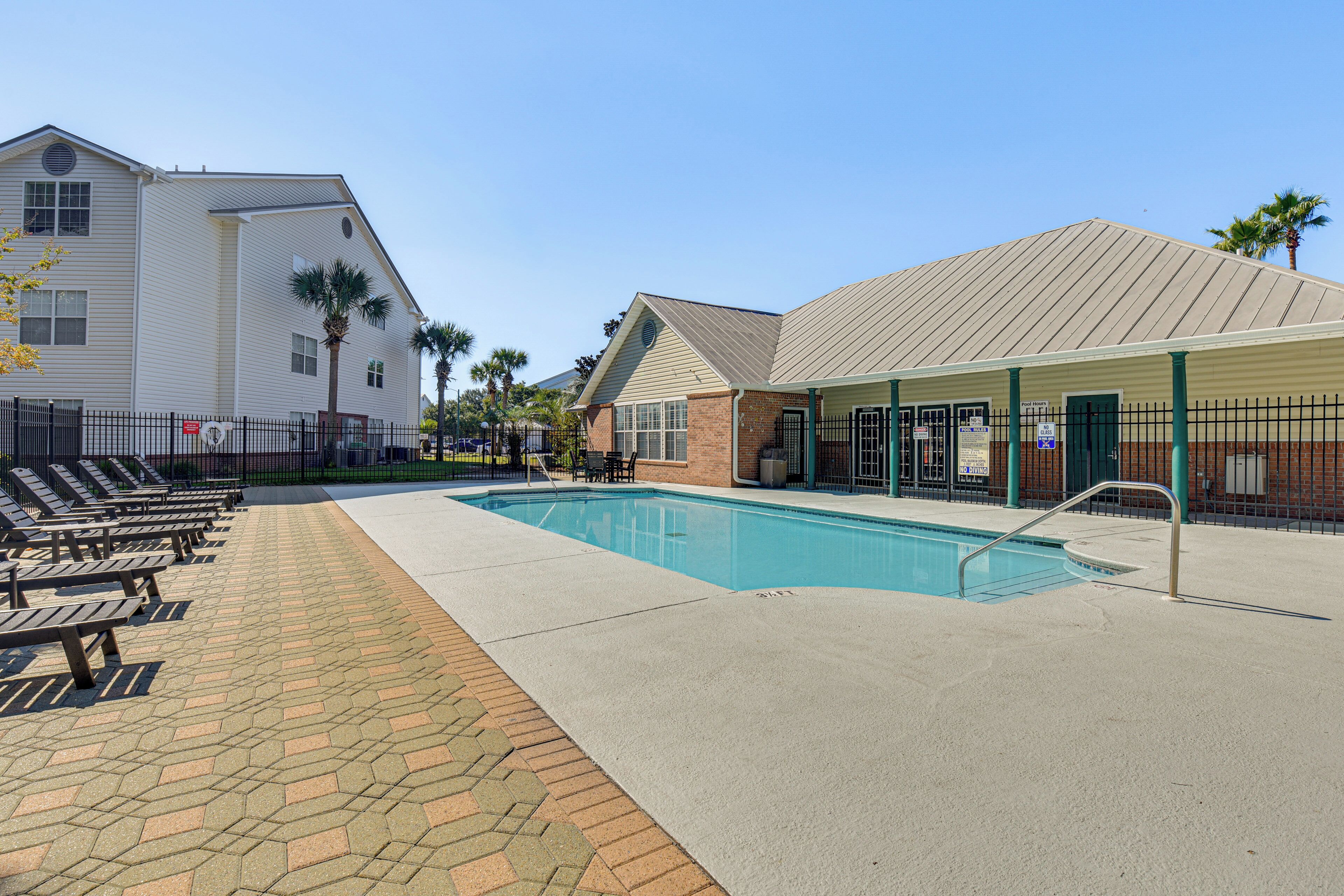 A swimming pool with lounge chairs and a covered area with pool rules signs.